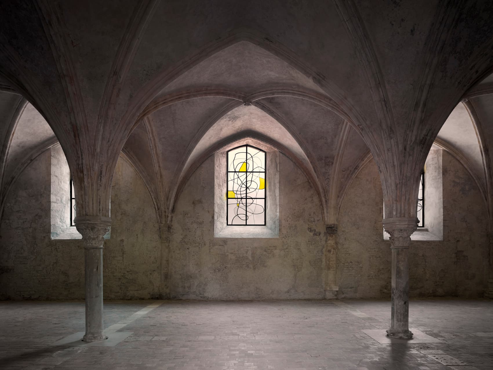 A color photograph of a cathedral-like space with vaulted ceilings. The image frames the space symmetrically, capturing three stained glass windows. The window at center of the image is stained glass that contrasts with the interior because of its contemporary design. Asymmetrical curved came outlines translucent glass pieces as well as four irregularly shaped yellow sections of glass.