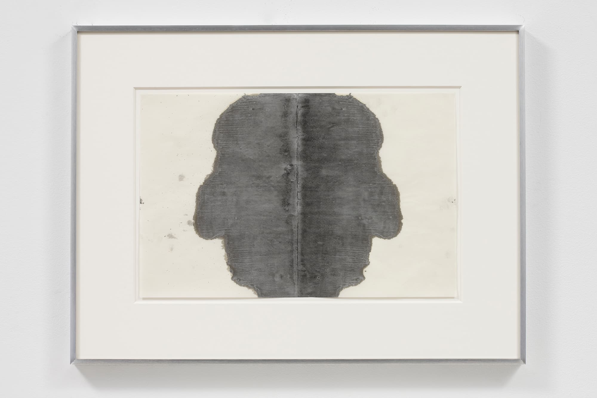 A color image of a framed black and white monoprint that looks like a rorschach test. The shapes suggest profiles facing outward.