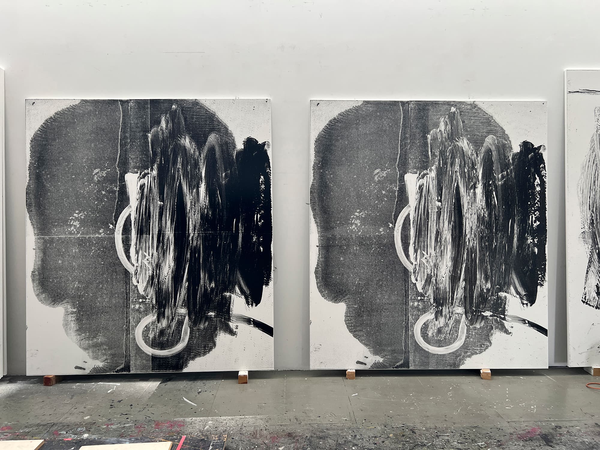 A color image of two nearly identical paintings. The works lean on a wall side-by-side. The overall form of each one alludes to a shape of a head with energetic vertical brushwork on the right half.